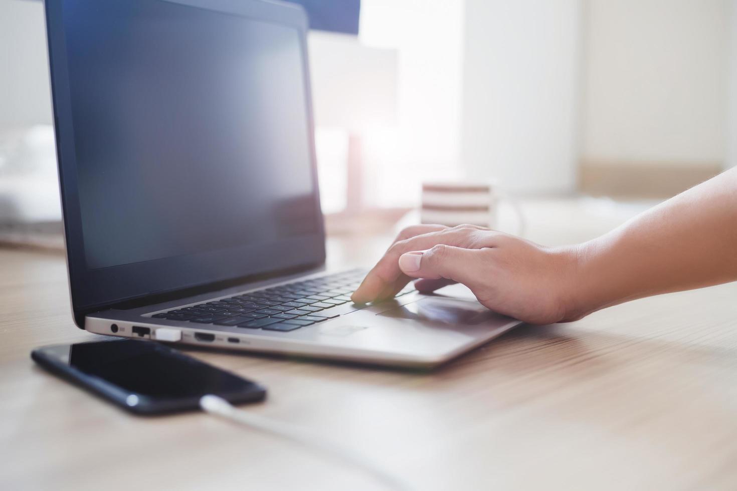 homem trabalhando com computador laptop e telefones inteligentes móveis cobrando na mesa de madeira background.work em casa pela manhã. foto