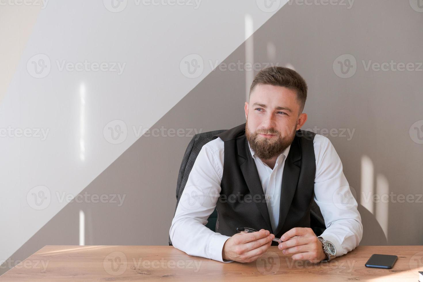 homem de negócios barbudo de retrato sentado no escritório meditando segurando a caneta na sua foto