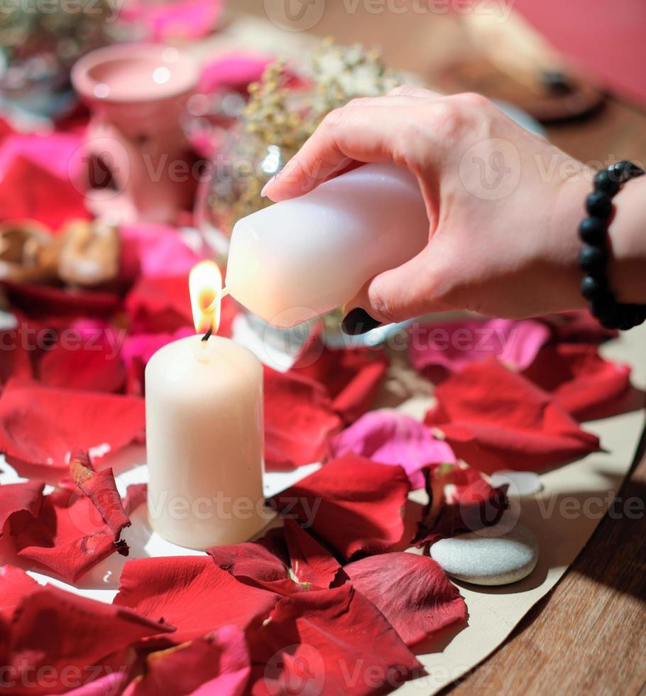 mulher acendendo uma vela sobre fundo de pétalas de rosa. pedras, ervas e velas durante a prática espiritual. rituais mágicos, sessão espírita e de canalização foto