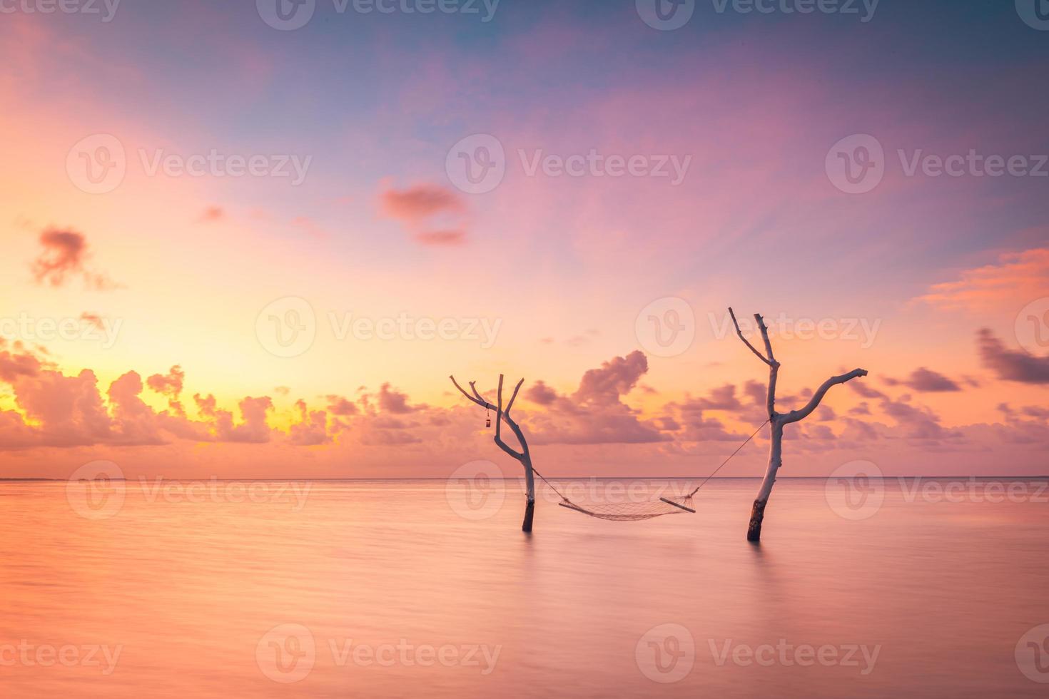 belo pôr do sol brilhante em uma praia paradisíaca tropical. abstrata longa exposição água e céu, galhos de árvores com balanço ou rede. lagoa incrível, costa da ilha, relaxamento, lazer lazer despreocupado foto