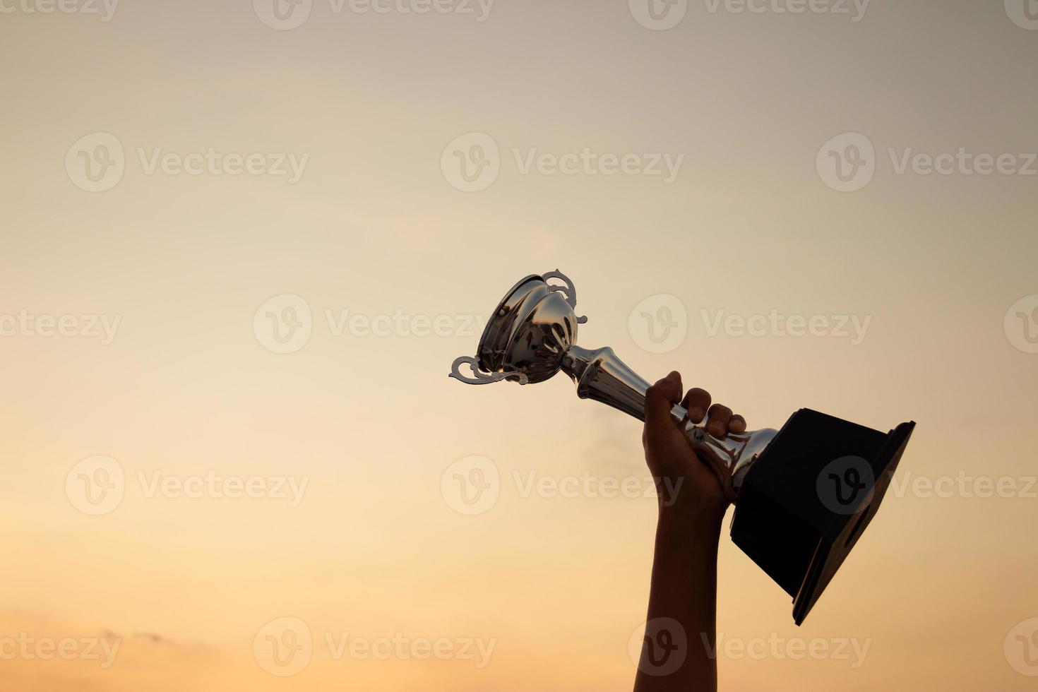 conceito de vitória com uma mão segurando um troféu no fundo do céu por do sol foto