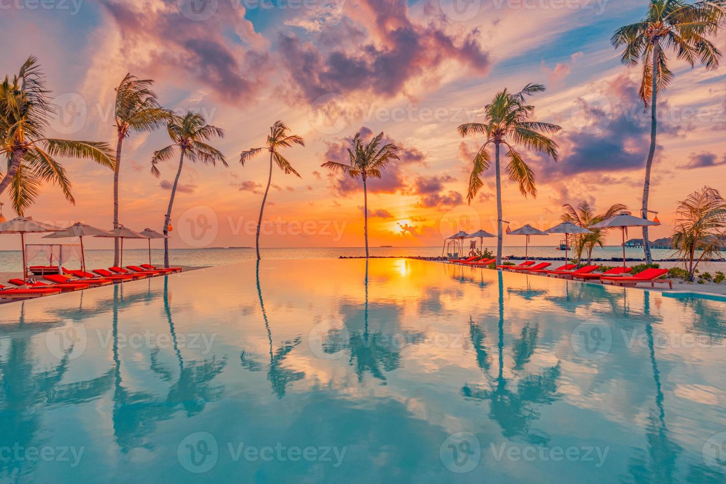 pôr do sol tropical sobre piscina infinita ao ar livre na estância balnear de verão, paisagem de praia. férias de praia tranquilas de luxo, reflexão à beira da piscina, espreguiçadeira relaxante céu colorido romântico, cadeiras guarda-chuva foto