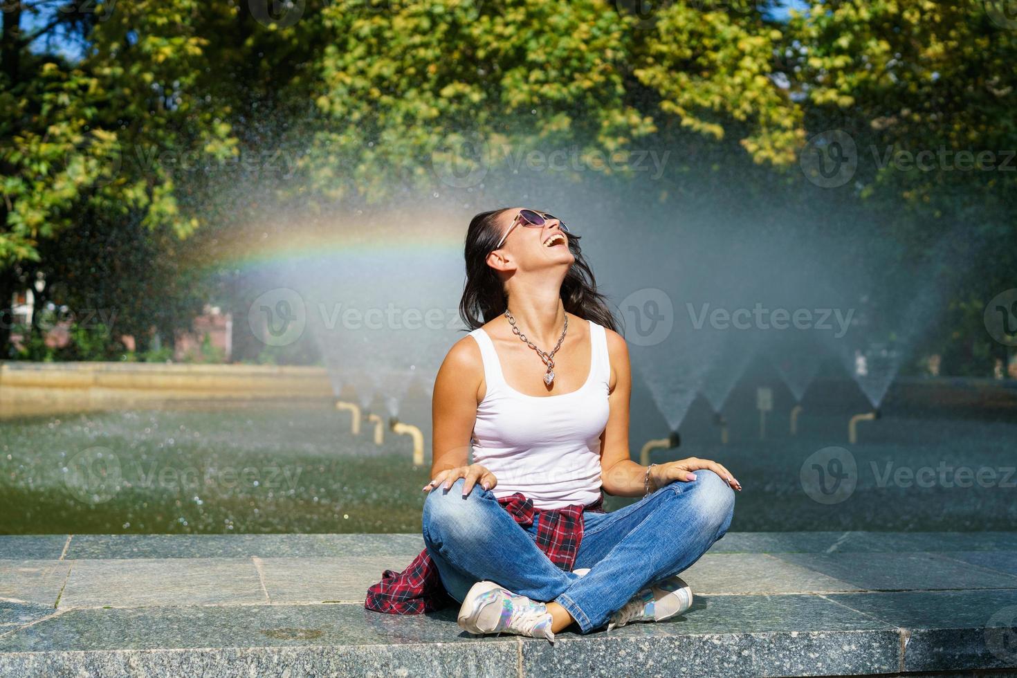 jovem caucasiana sentada perto da fonte gosta de frescura da água no sol foto