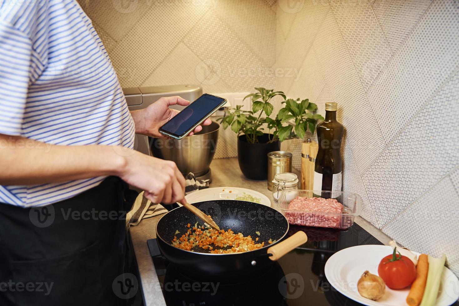 mulher cozinhando molho à bolonhesa e use smartphone foto