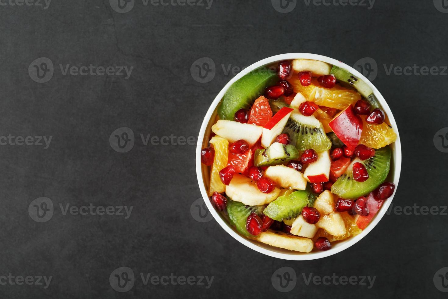 salada de frutas em um copo branco em um fundo preto, espaço livre para texto. foto