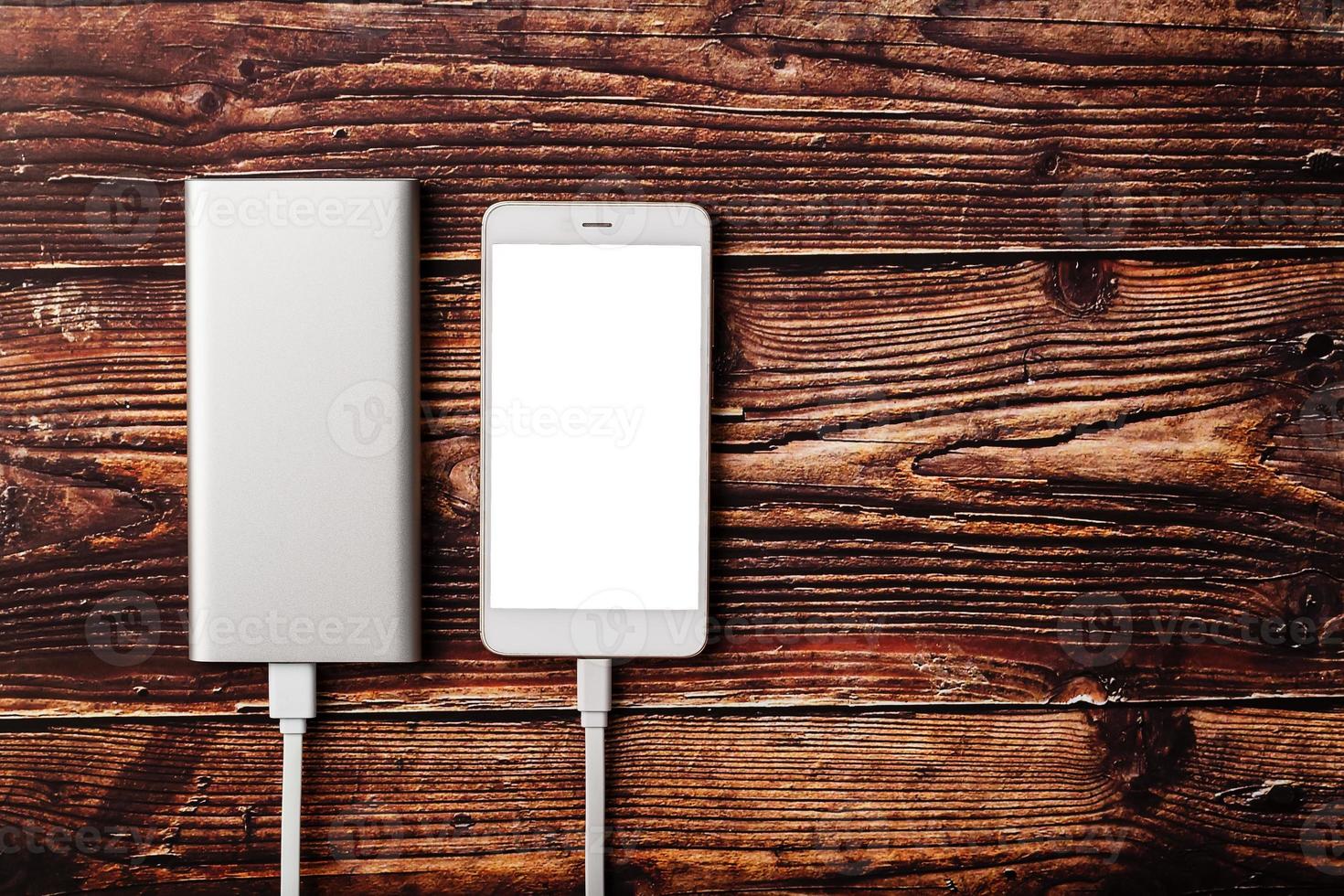 powerbank carrega um smartphone em um fundo de madeira. bateria externa universal para gadgets espaço livre e composição minimalista. foto