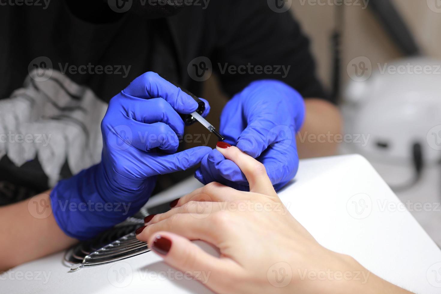 mestre em luvas de proteção durante uma manicure no salão de beleza. mestre manicure enverniza o gel marsala nas unhas de uma cliente do sexo feminino. o conceito de beleza e saúde. foto