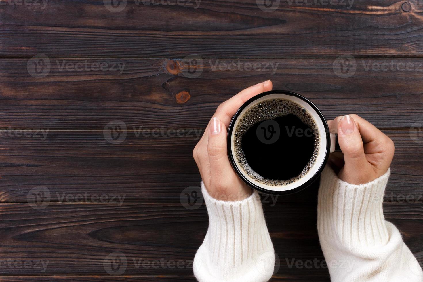 mulher solitária tomando café da manhã, vista superior das mãos femininas segurando um copo de bebida quente na mesa de madeira foto