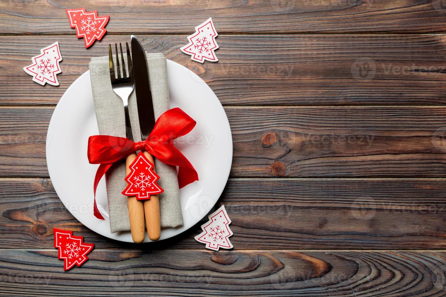 vista superior do prato, garfo e faca servido no fundo de madeira decorado de natal. conceito de véspera de ano novo com espaço de cópia foto