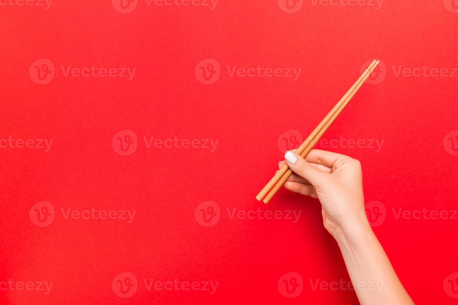 corte a imagem da mão feminina segurando os pauzinhos sobre fundo vermelho. conceito de comida japonesa com espaço de cópia foto