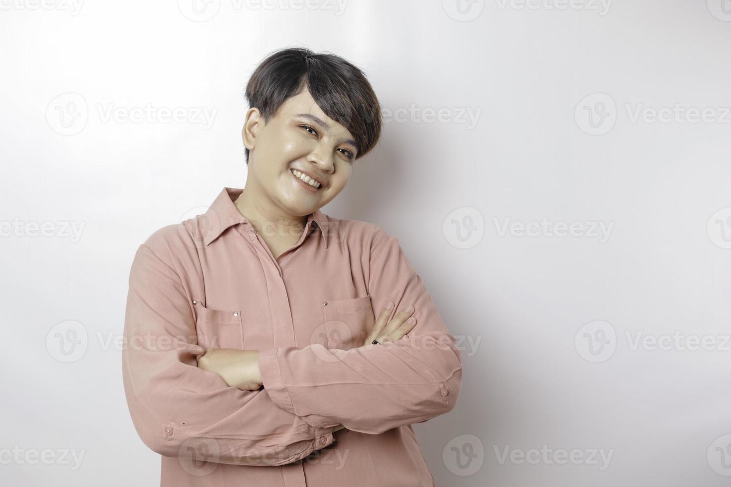 retrato de uma mulher asiática sorridente confiante vestindo camisa rosa em pé com os braços cruzados e olhando para a câmera isolada sobre fundo branco foto