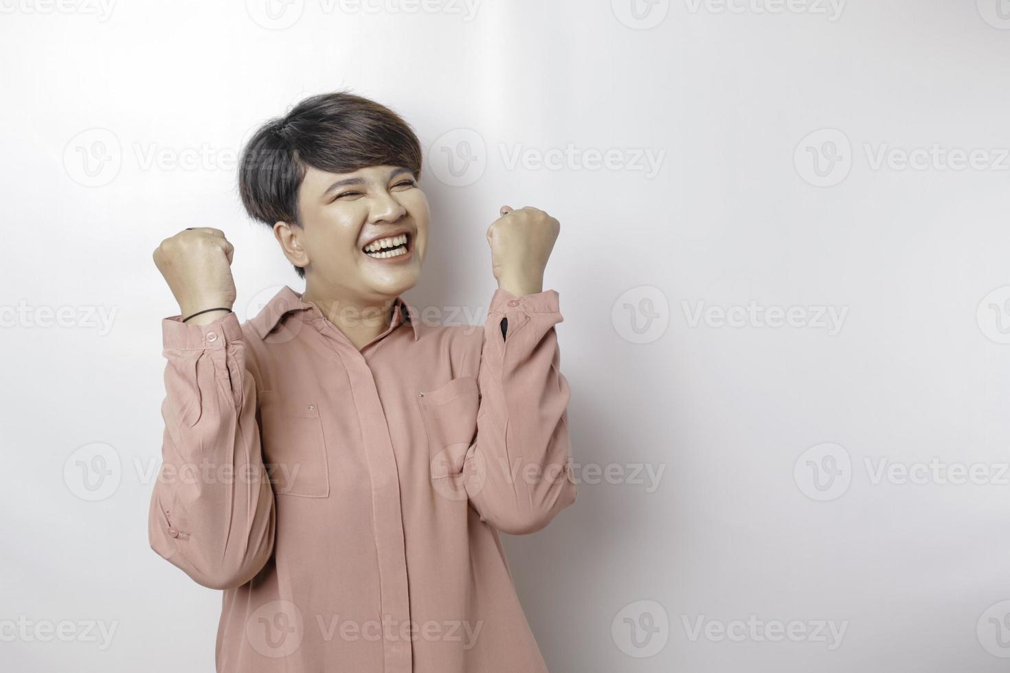 uma jovem mulher asiática de cabelos curtos com uma expressão feliz e bem sucedida vestindo uma camisa rosa isolada por um fundo branco foto