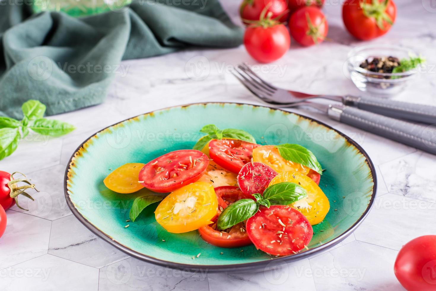 tomates vermelhos e amarelos fatiados e folhas de manjericão em um prato na mesa foto