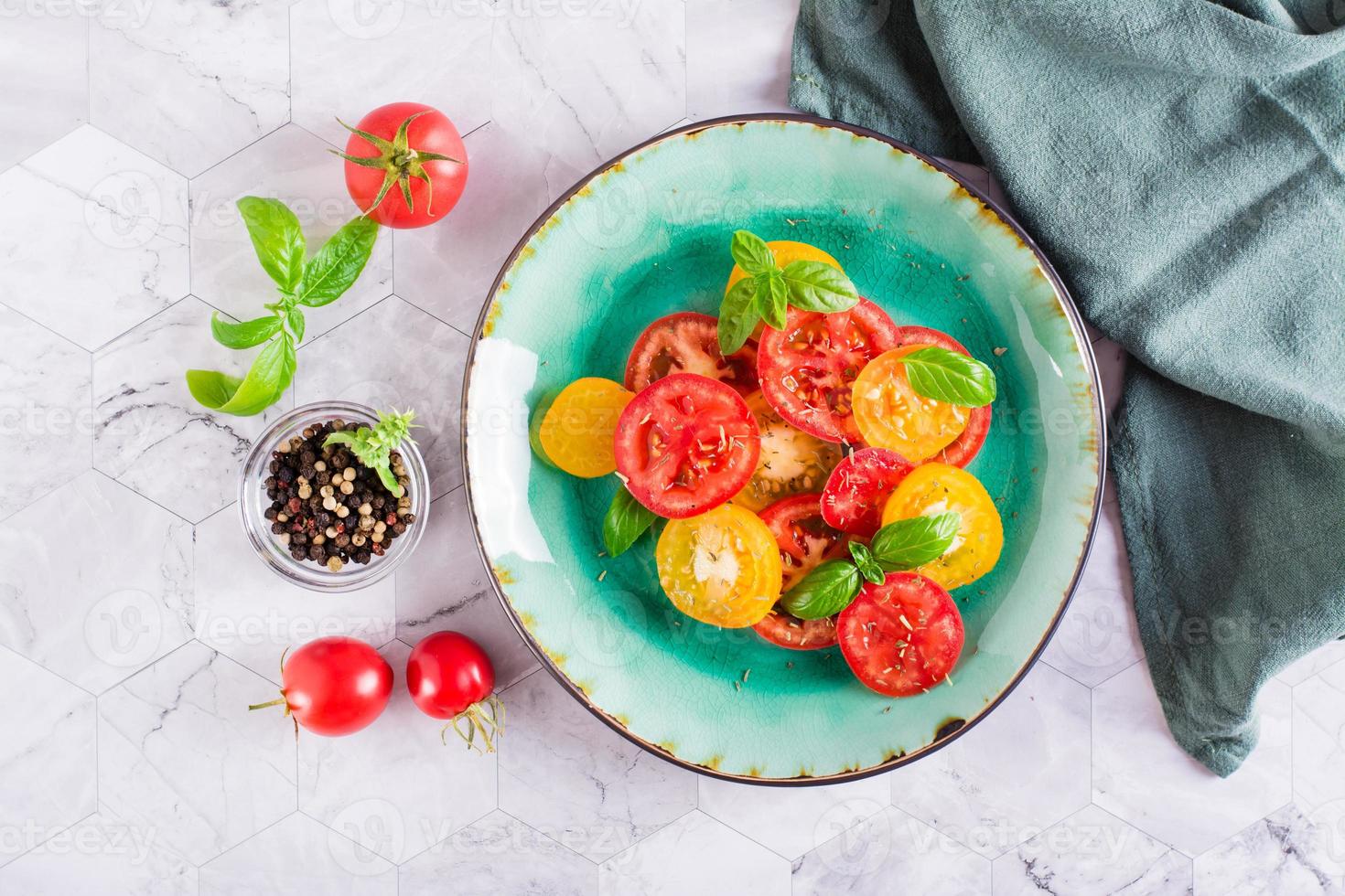 salada fresca de tomates amarelos e vermelhos com folhas de manjericão em um prato na mesa. vista do topo foto