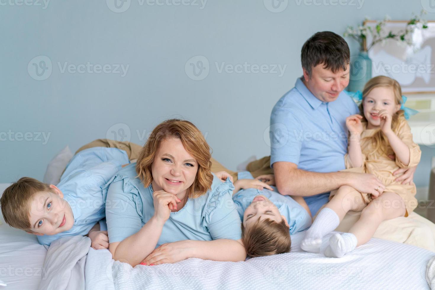 família feliz olhando para a câmera em sua cama no quarto. pais caucasianos foto