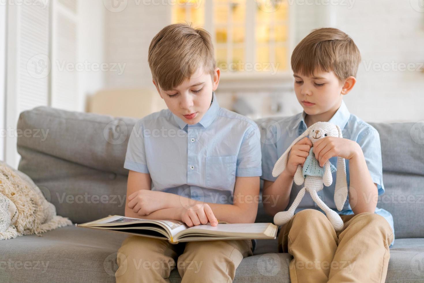 dois meninos sentados no sofá estão lendo o livro. irmão mais velho lê interessante foto