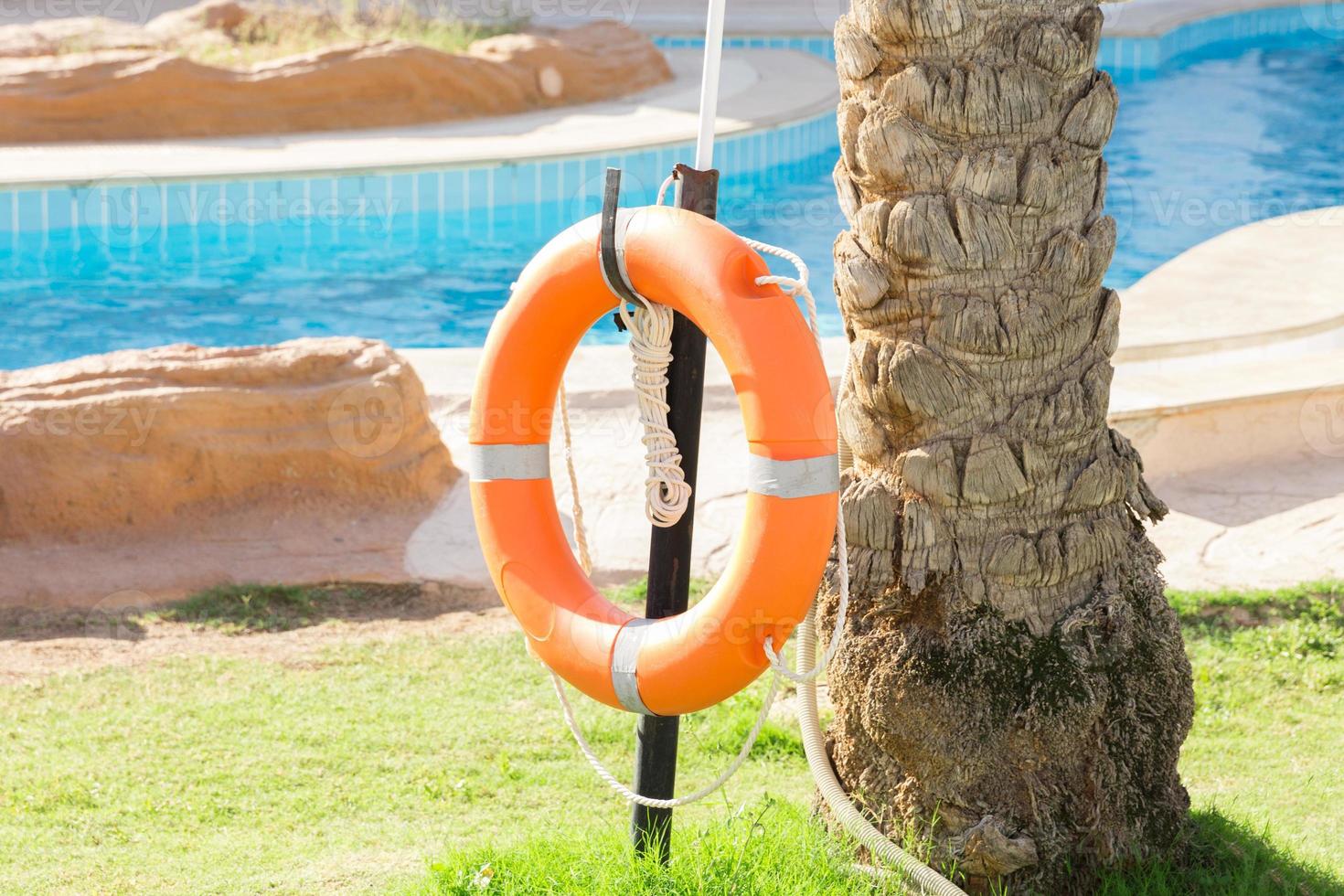 bóia salva-vidas de emergência laranja pendurada na cerca perto da piscina de férias no hotel foto