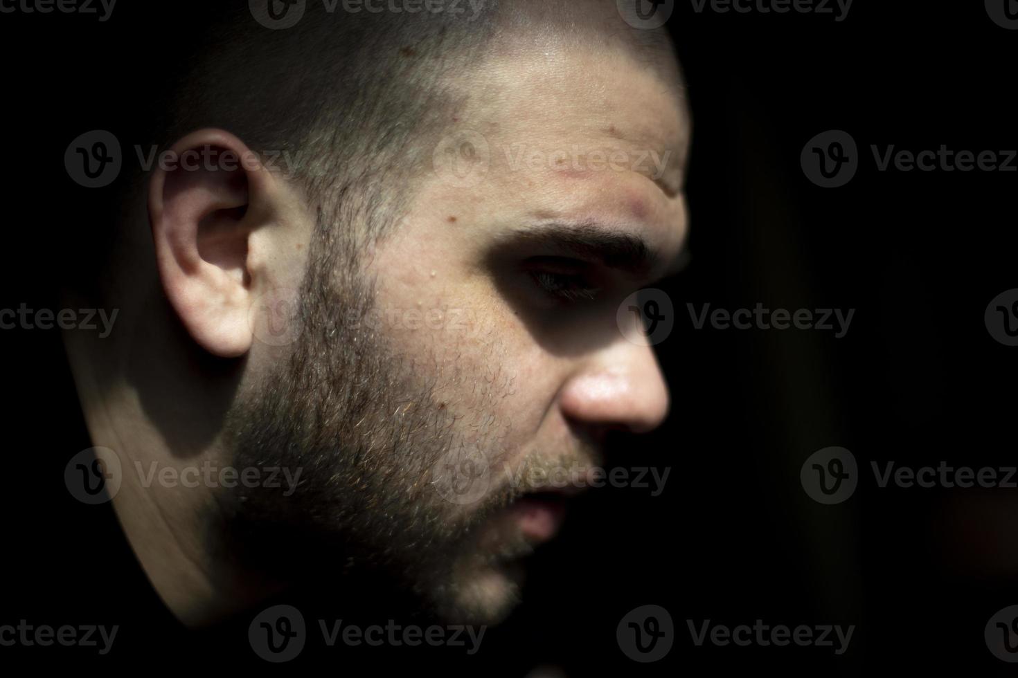 cara de cara está em fundo preto. homem na luz. vista lateral de cara jovem. foto