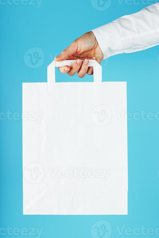 saco de papel no comprimento do braço, saco de artesanato branco para takeaway isolado em fundo azul. layout de modelo de embalagem com espaço para cópia, publicidade. foto