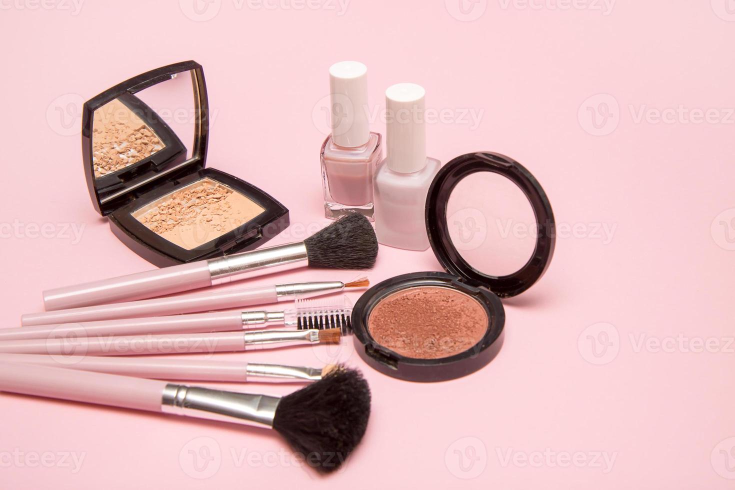 pincéis de maquiagem, pó, blush, esmalte em um fundo rosa, o conceito de tudo para maquiagem, acessórios cosméticos foto