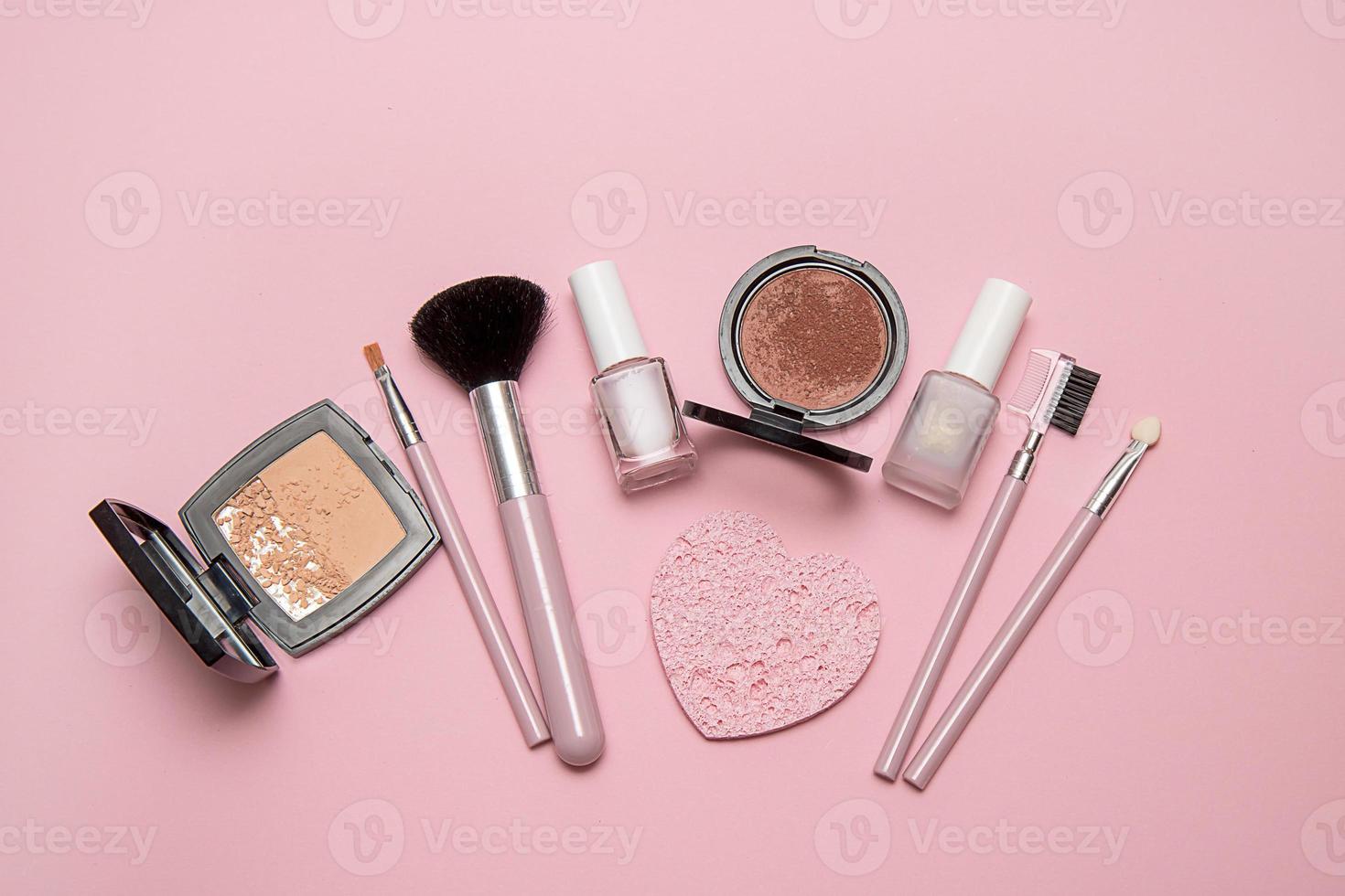 escovas cosméticas, pó, blush, esmalte em fundo rosa foto