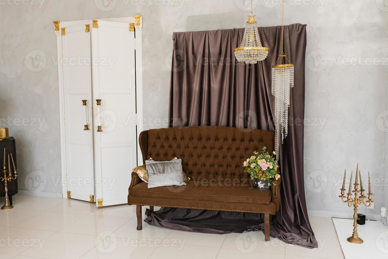 um luxuoso sofá clássico marrom com almofadas e um buquê de flores em um vaso, um lustre de cristal e portas brancas para um quarto na sala de estar da casa foto