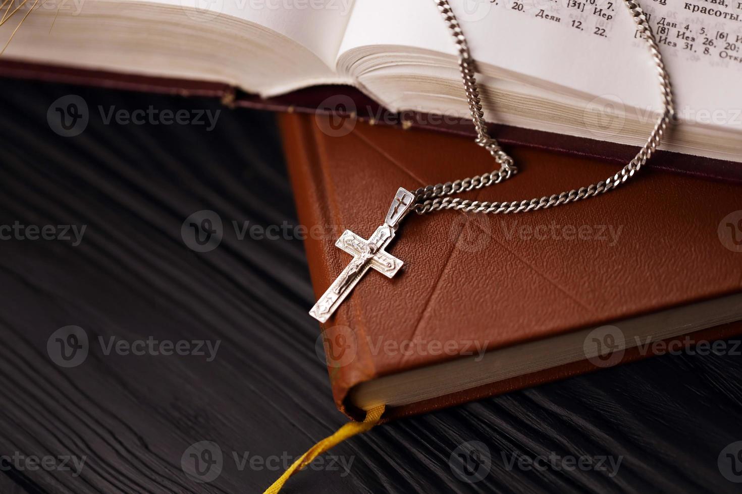 colar de prata com cruz crucifixo no livro da bíblia sagrada cristão na mesa de madeira preta. pedindo bênçãos de deus com o poder da santidade, que traz sorte foto