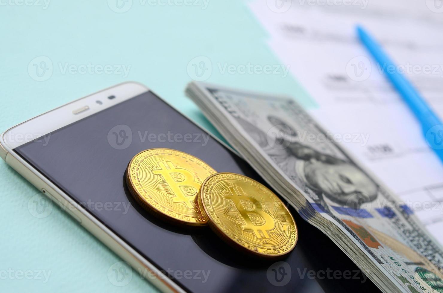 bitcoins encontra-se com os formulários de imposto, notas de cem dólares e smartphone em um fundo azul claro. restituição do Imposto de Renda foto