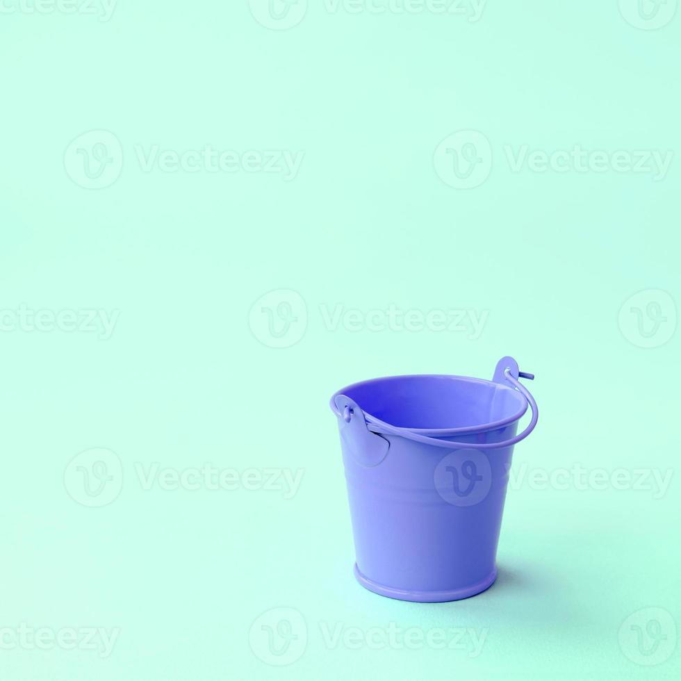 um balde lilás vazio em miniatura encontra-se em um fundo verde pastel foto
