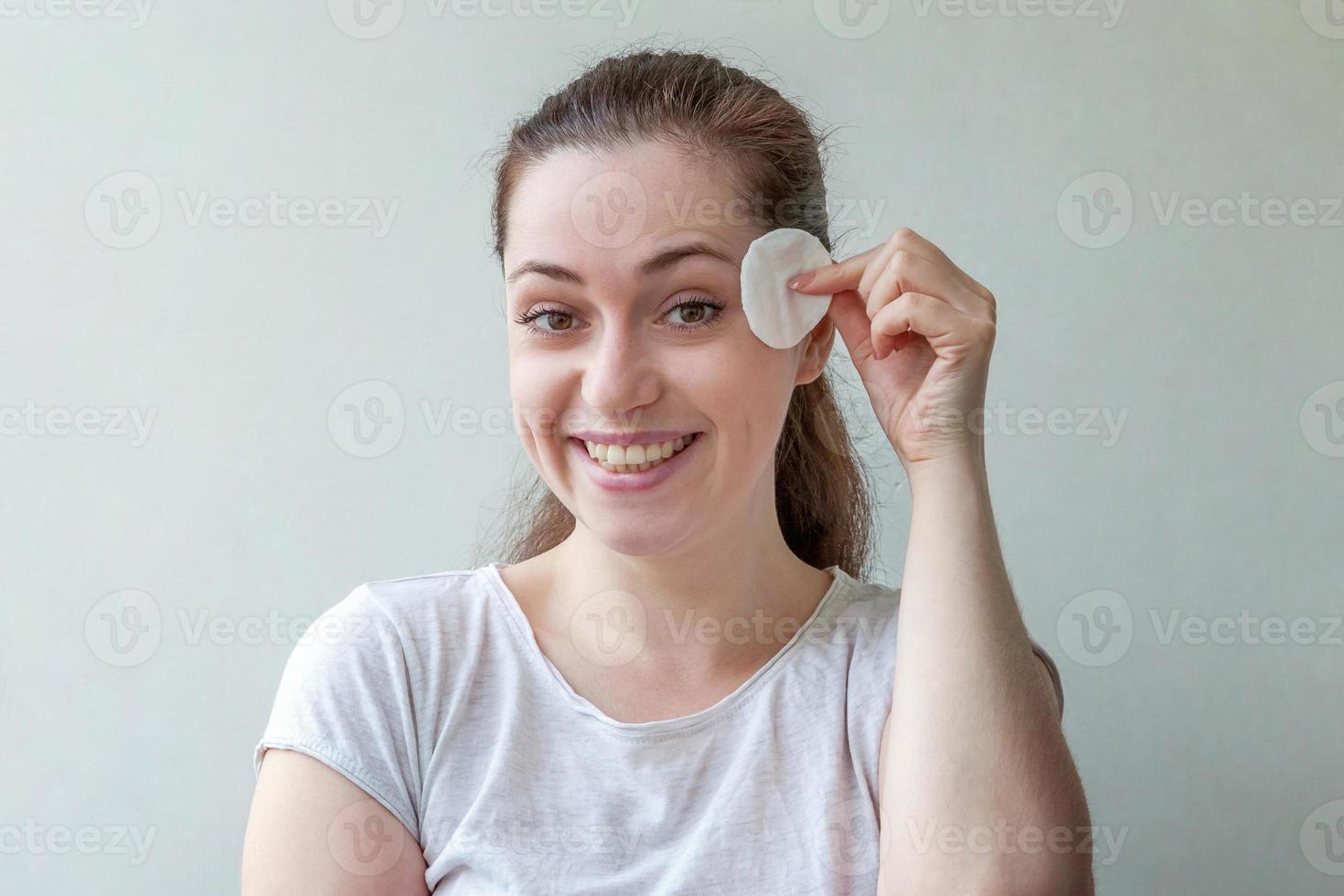 mulher sorridente com pele macia e saudável, removendo a maquiagem com almofada de algodão isolada no fundo branco foto