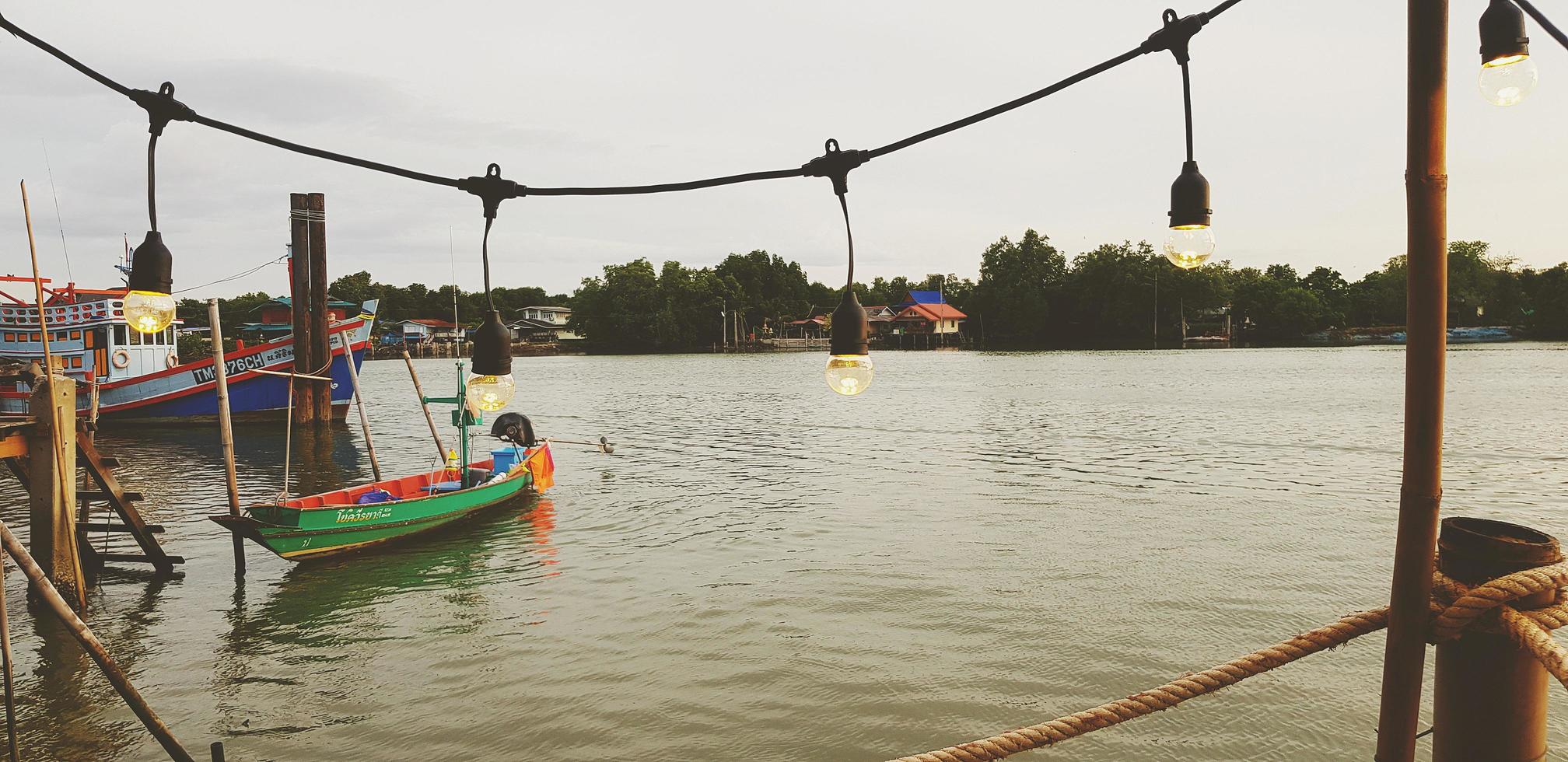 samut sakhon, tailândia - 15 de julho de 2022 barco de cauda longa verde no rio com iluminação de primeiro plano e céu, verde com fundo doméstico em tom vintage. estilo de vida rural com vista para a natureza e a paisagem. foto
