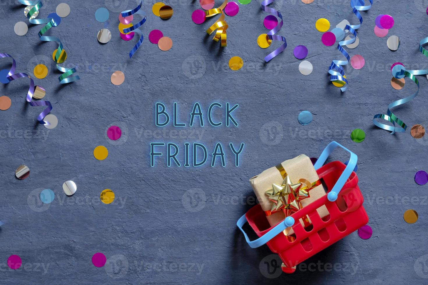 sexta-feira preta tetx com cesta de compras e enfeites festivos deitado em fundo escuro. vista do topo foto