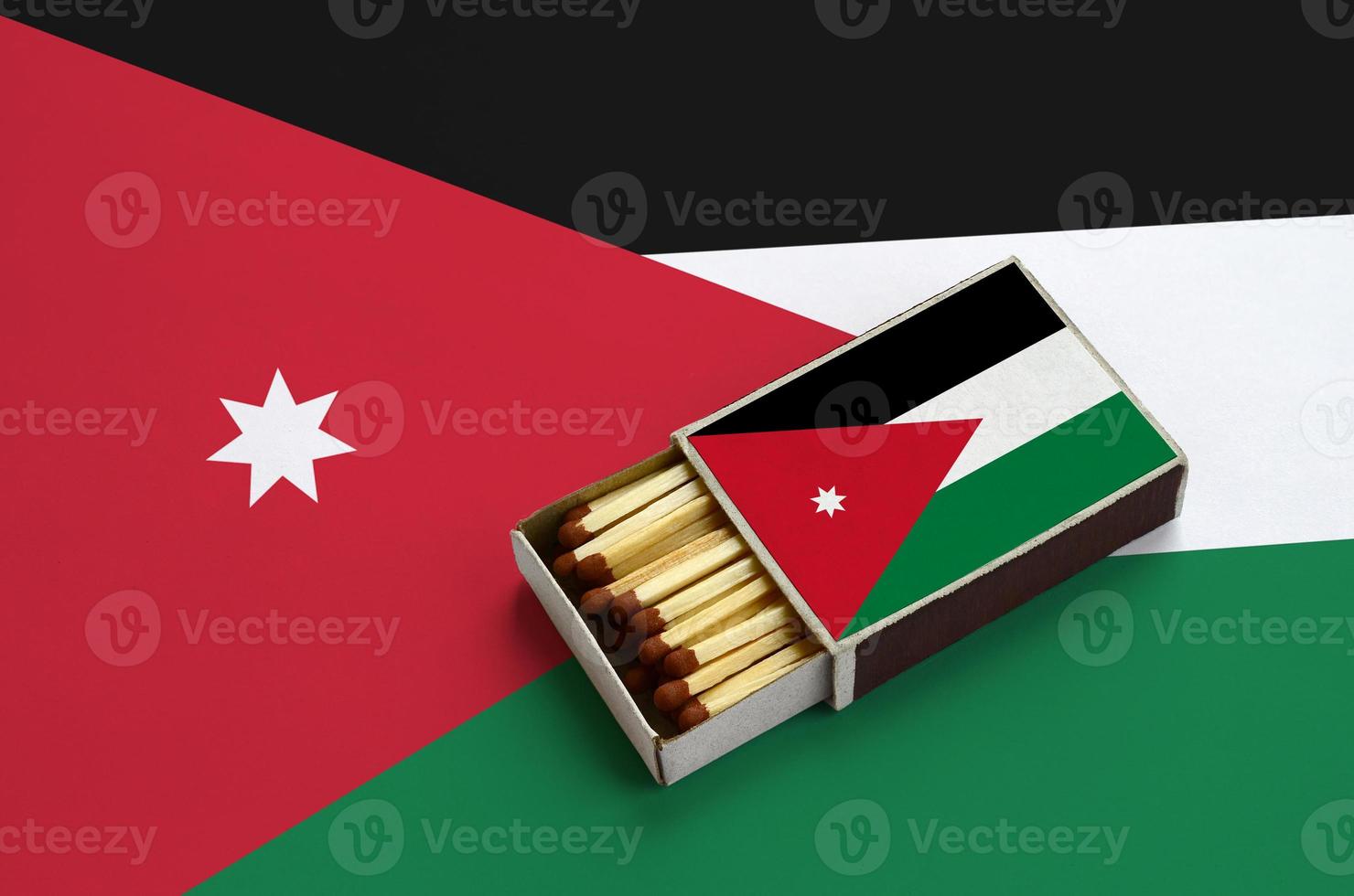 A bandeira da Jordânia é mostrada em uma caixa de fósforos aberta, cheia de fósforos e em uma grande bandeira foto