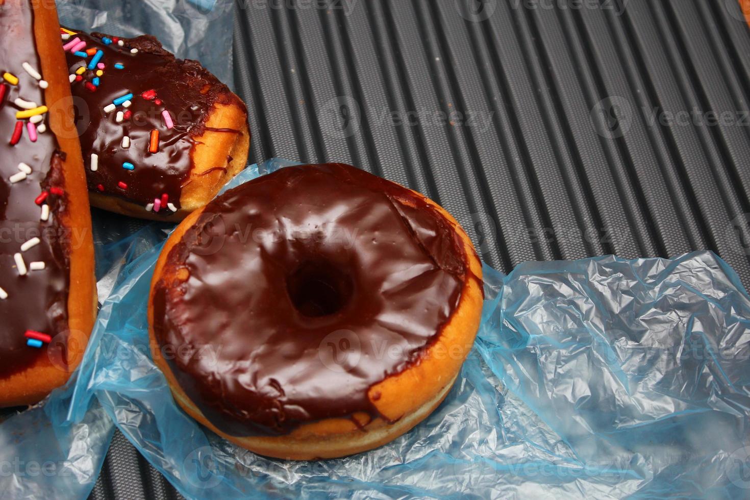 rosquinhas de chocolate e barras de donuts de chocolate cobertas com flocos de açúcar multicoloridos. colocado em um piso de alumínio cinza. foto