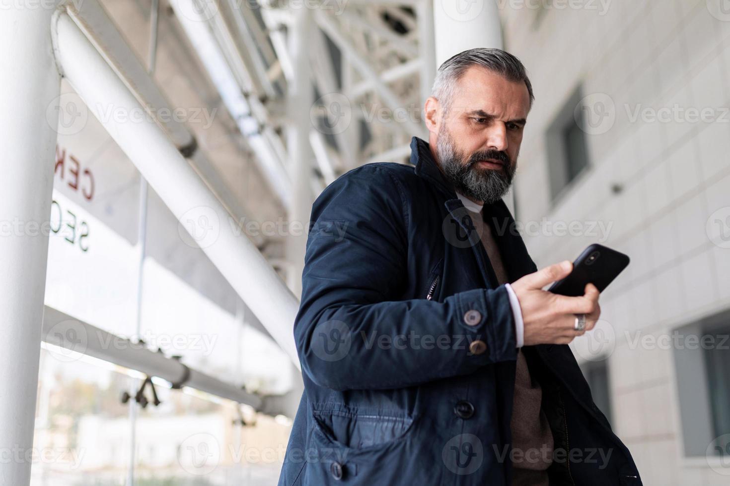 homem maduro esperando para embarcar em um voo no aeroporto olhando para seu celular foto