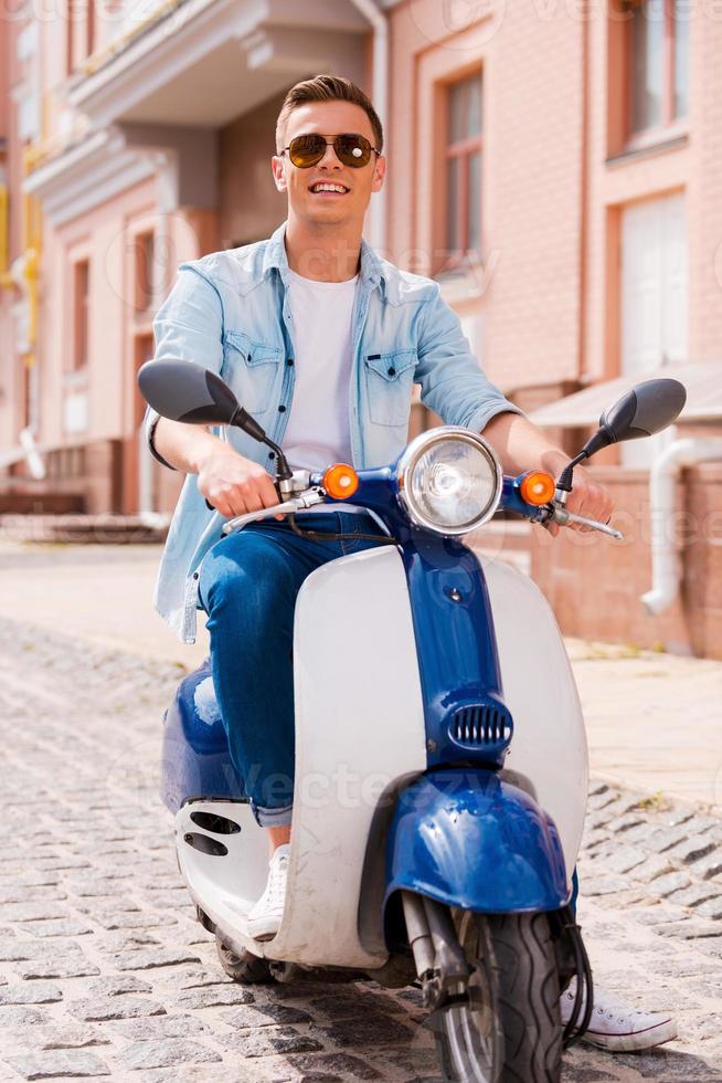 pronto para montar. jovem bonito andando de scooter ao longo da rua e sorrindo foto