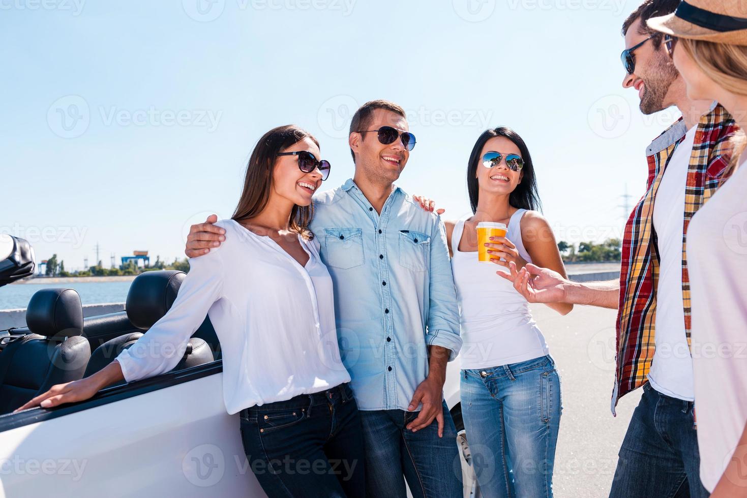 passar bons momentos com os amigos. grupo de jovens felizes conversando entre si e sorrindo em pé perto de seu conversível foto