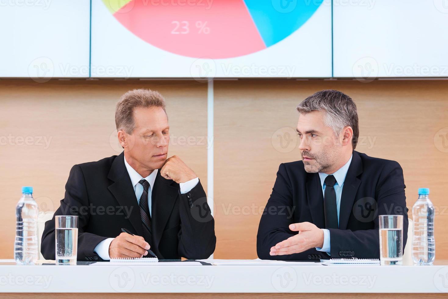 preparando para apresentação. dois empresários confiantes em trajes formais discutindo algo com grande monitor sobre eles foto