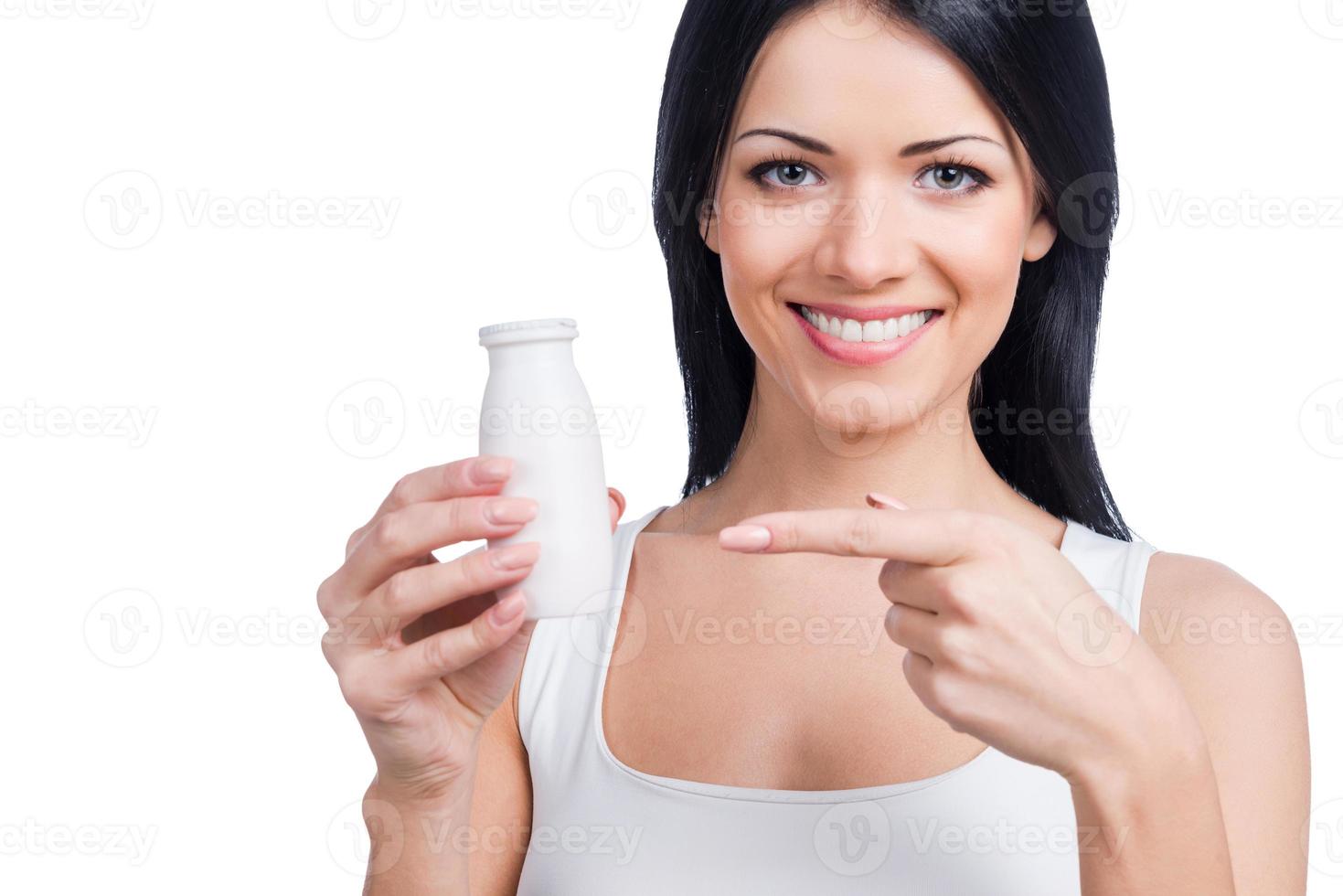 bebida da saúde. bela jovem sorridente segurando uma garrafa e apontando para ela em pé contra um fundo branco foto