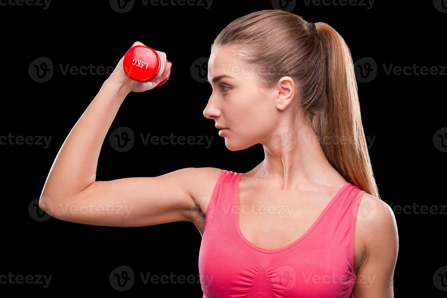 mantendo seu corpo em forma. jovem esportiva exercitando com haltere em pé contra um fundo preto foto