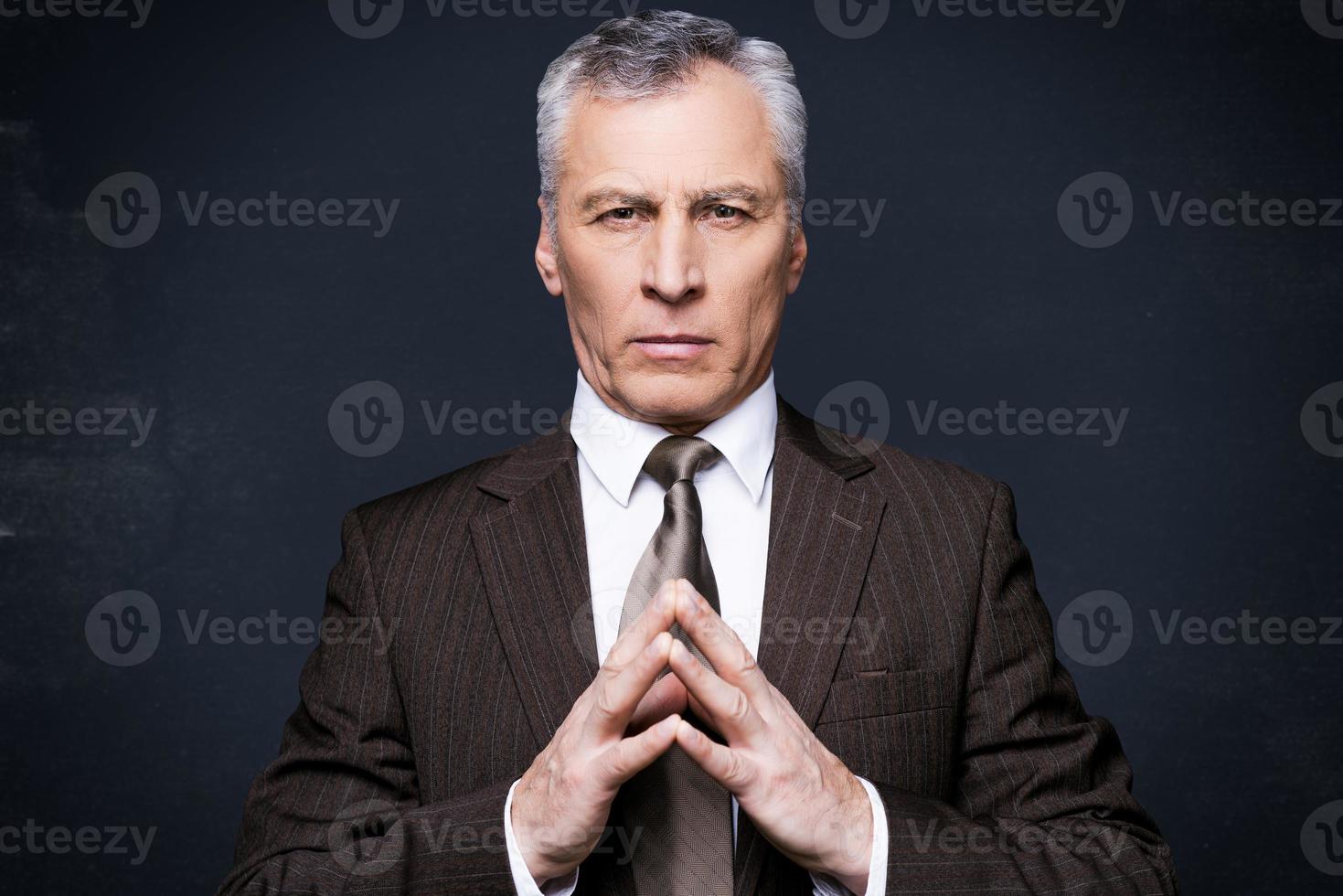 o poder está em suas mãos. retrato de homem sênior confiante em traje formal, olhando para a câmera em pé contra o quadro-negro foto