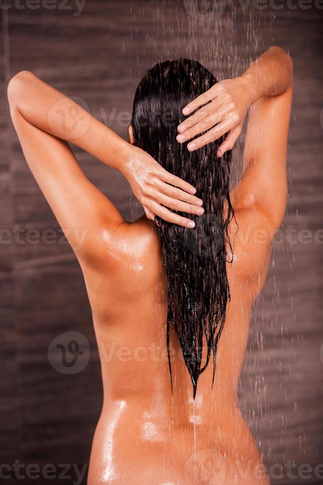 refrescando seu corpo. vista traseira da bela jovem nua em pé no chuveiro e lavando o cabelo foto