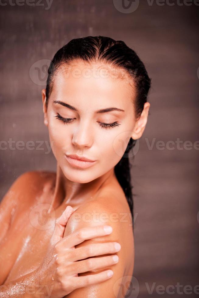 beleza no chuveiro. bela jovem sem camisa em pé no chuveiro e lavando o ombro foto