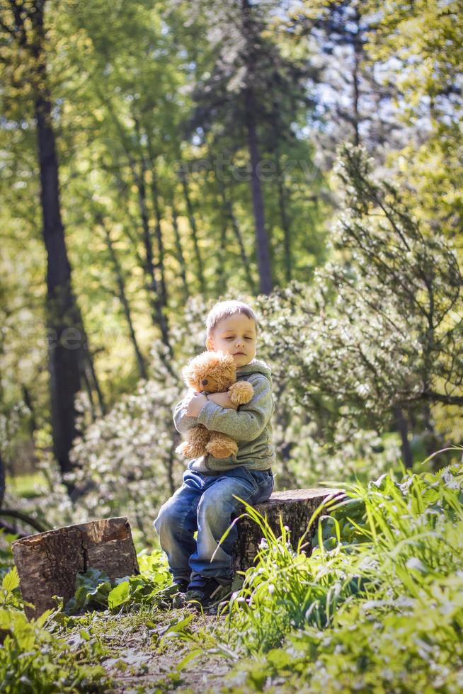 um menino bonito está brincando com um filhote de urso na floresta. os raios do sol envolvem o espaço da clareira com um toco. uma história mágica de interações para o livro. espaço para copiar. seletivo foto