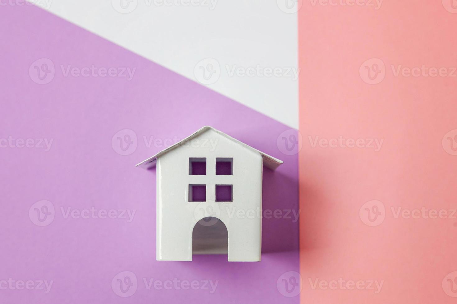 simplesmente projete com casa de brinquedo branca em miniatura isolada em fundo geométrico na moda colorido pastel rosa violeta branco. conceito de casa de sonho de seguro de propriedade de hipoteca. espaço de cópia de vista superior plana leiga. foto