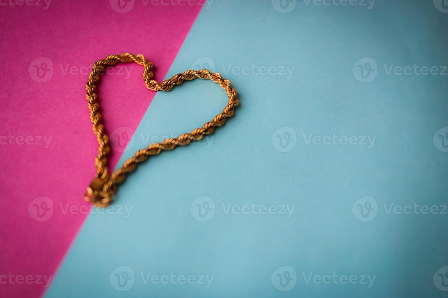 textura de uma bela cadeia festiva dourada tecelagem única em forma de coração em um fundo azul roxo rosa e espaço de cópia. conceito de amor, proposta de casamento, casamento, st. Dia dos Namorados foto