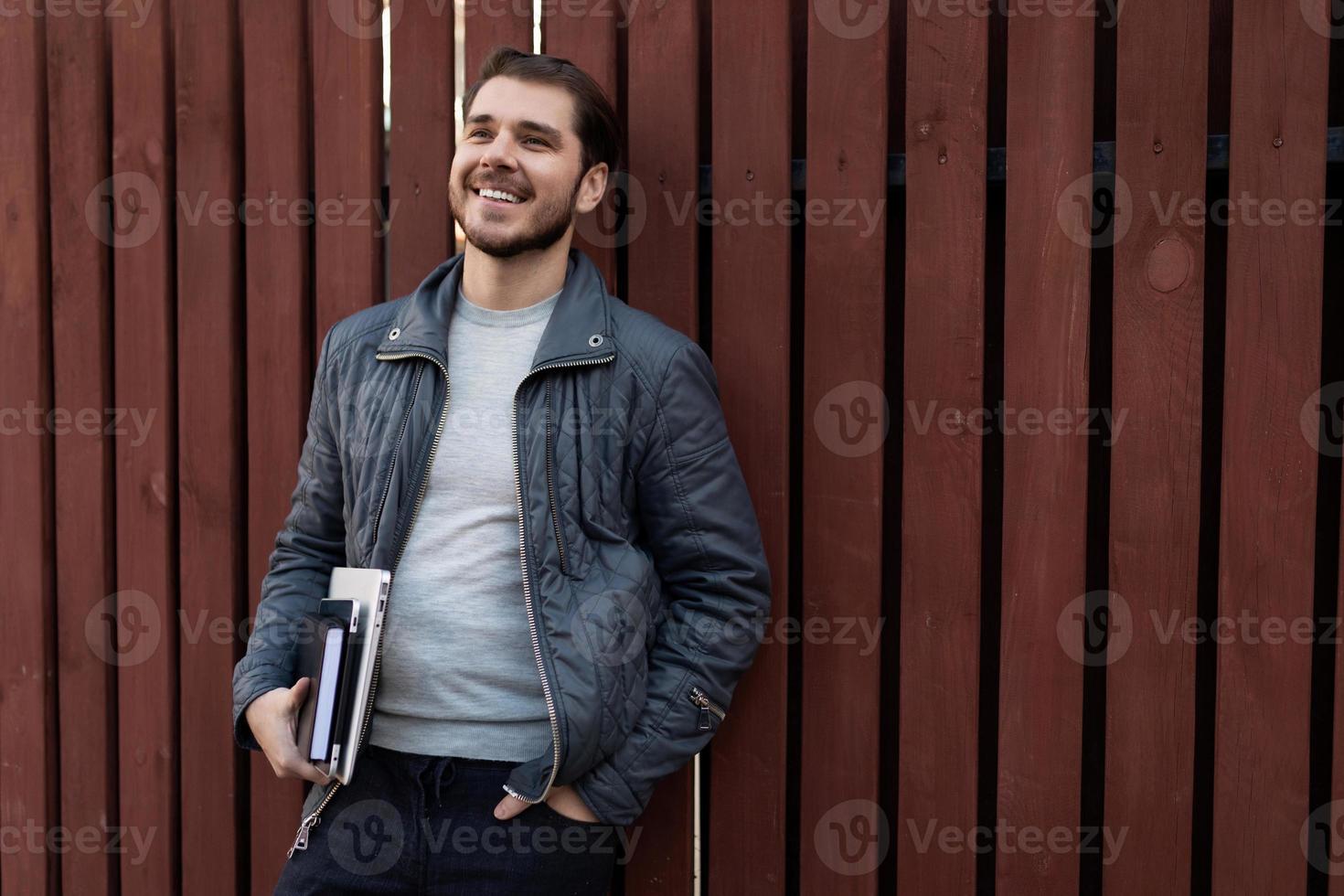 homem de negócios feliz com um laptop nas mãos no fundo de uma cerca de madeira marrom foto