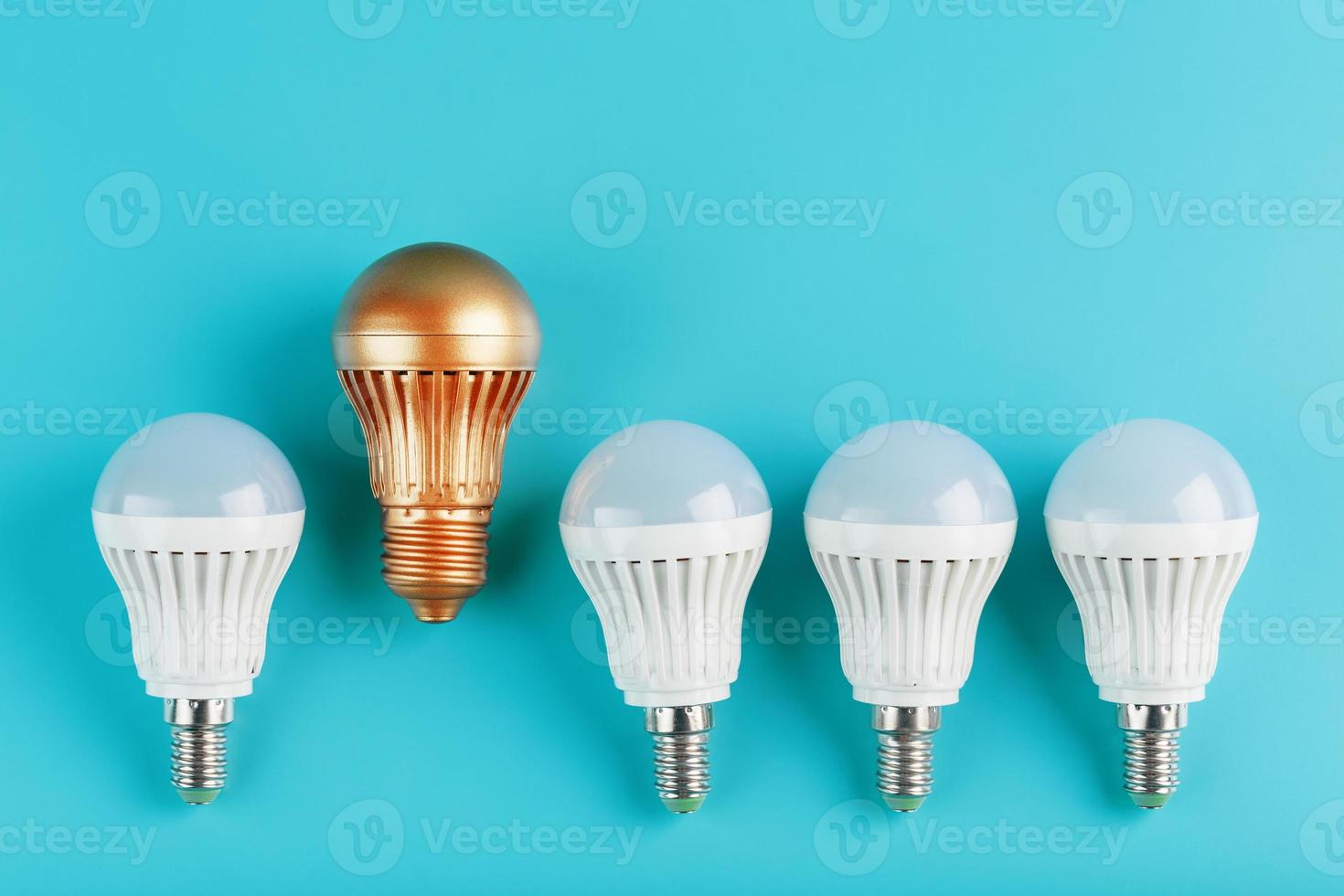 uma lâmpada led dourada é mais alta e se destaca de uma fileira de lâmpadas brancas em um fundo azul. foto