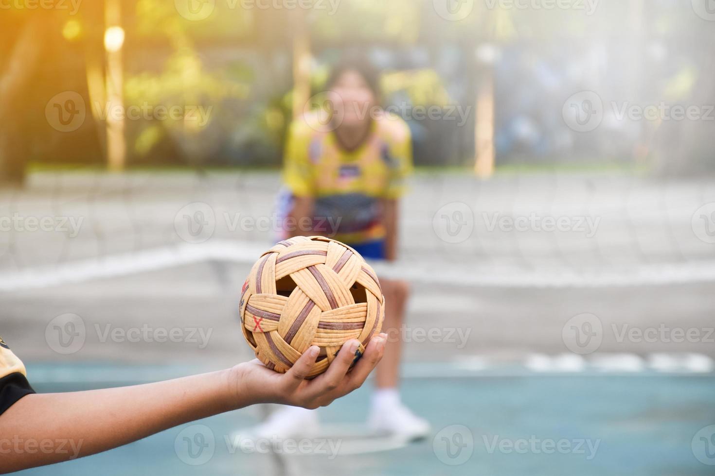 bola sepak takraw, esporte tradicional dos países do sudeste asiático, segurando na mão do jovem jogador sepak takraw feminino asiático na frente da rede antes de jogá-lo para outro jogador para chutar a rede. foto