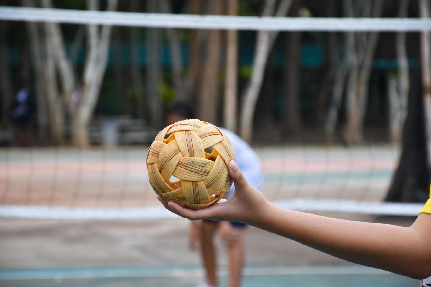 bola sepak takraw, esporte tradicional dos países do sudeste asiático, segurando na mão do jovem jogador sepak takraw feminino asiático na frente da rede antes de jogá-lo para outro jogador para chutar a rede. foto